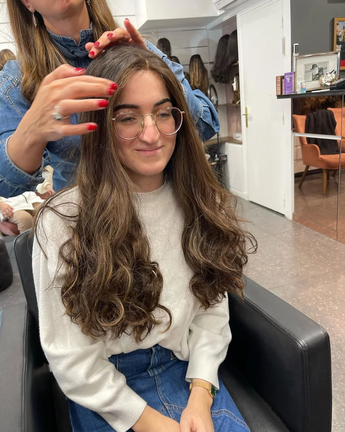 Mains de la perruquière au travail dans une longue chevelure bouclée en cheveux naturels