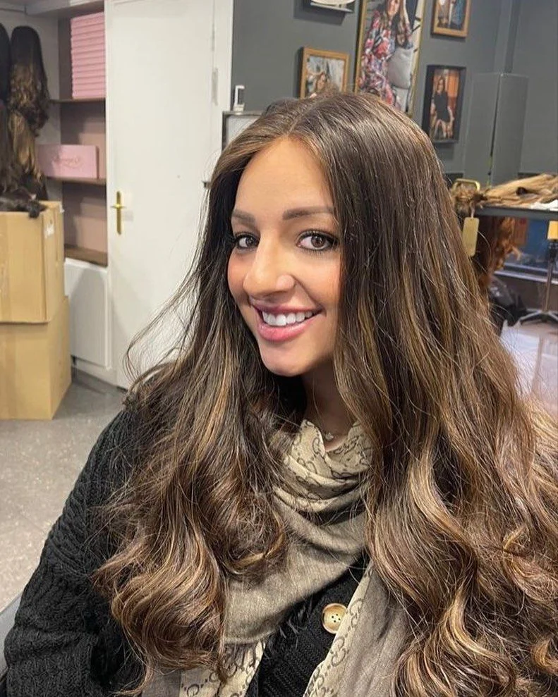 Cliente souriante portant une perruque longue brune au balayage caramel, raie au milieu
