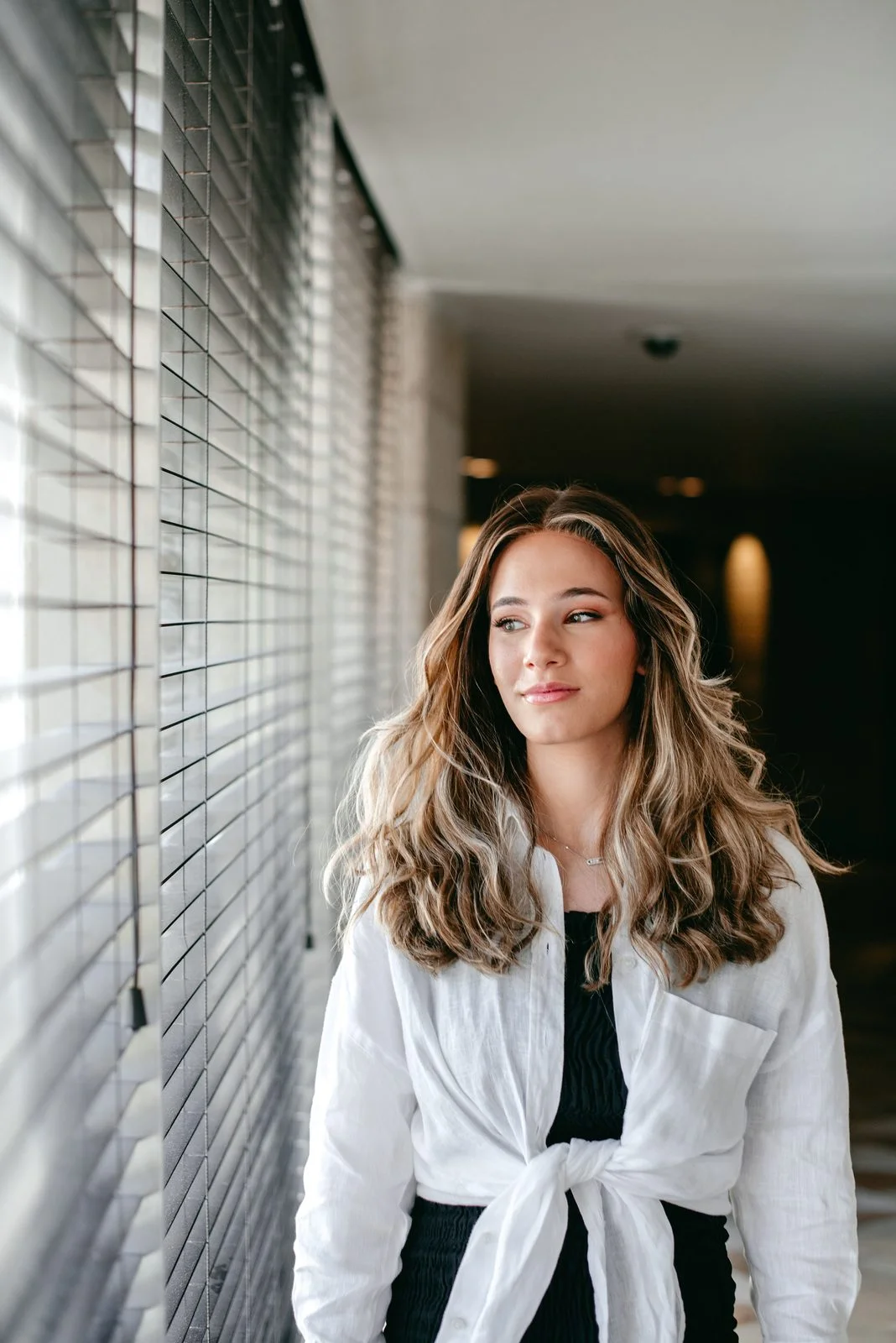 Perruque longue blond balayage en cheveux naturels, ondulations souples portées en chemise blanche